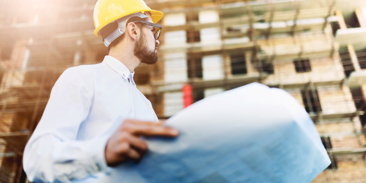 Man in hard hat looking at blueprints in from on construction site